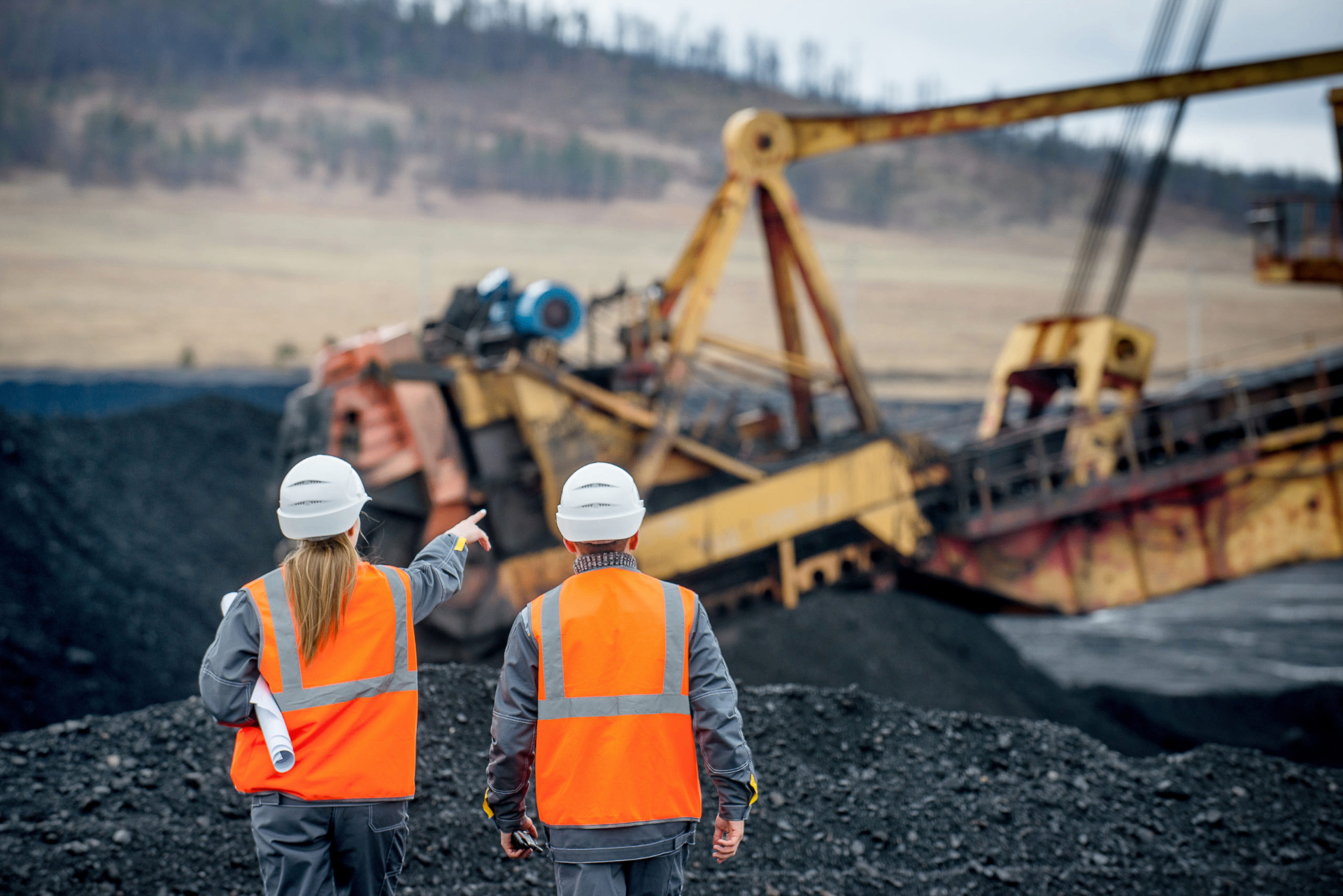 Two workers in high-visibility vests and hard hats observing heavy mining equipment at an open-pit site